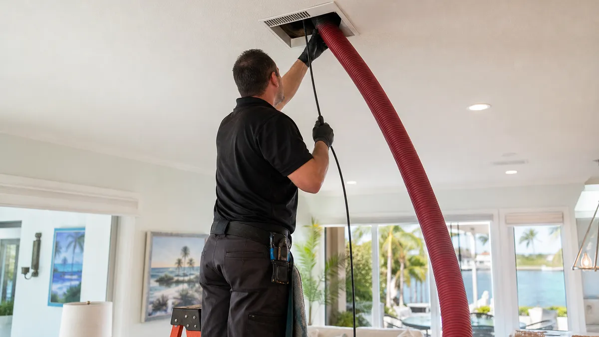 Technician using negative-pressure equipment to source-clean ducts, coil, and blower wheel